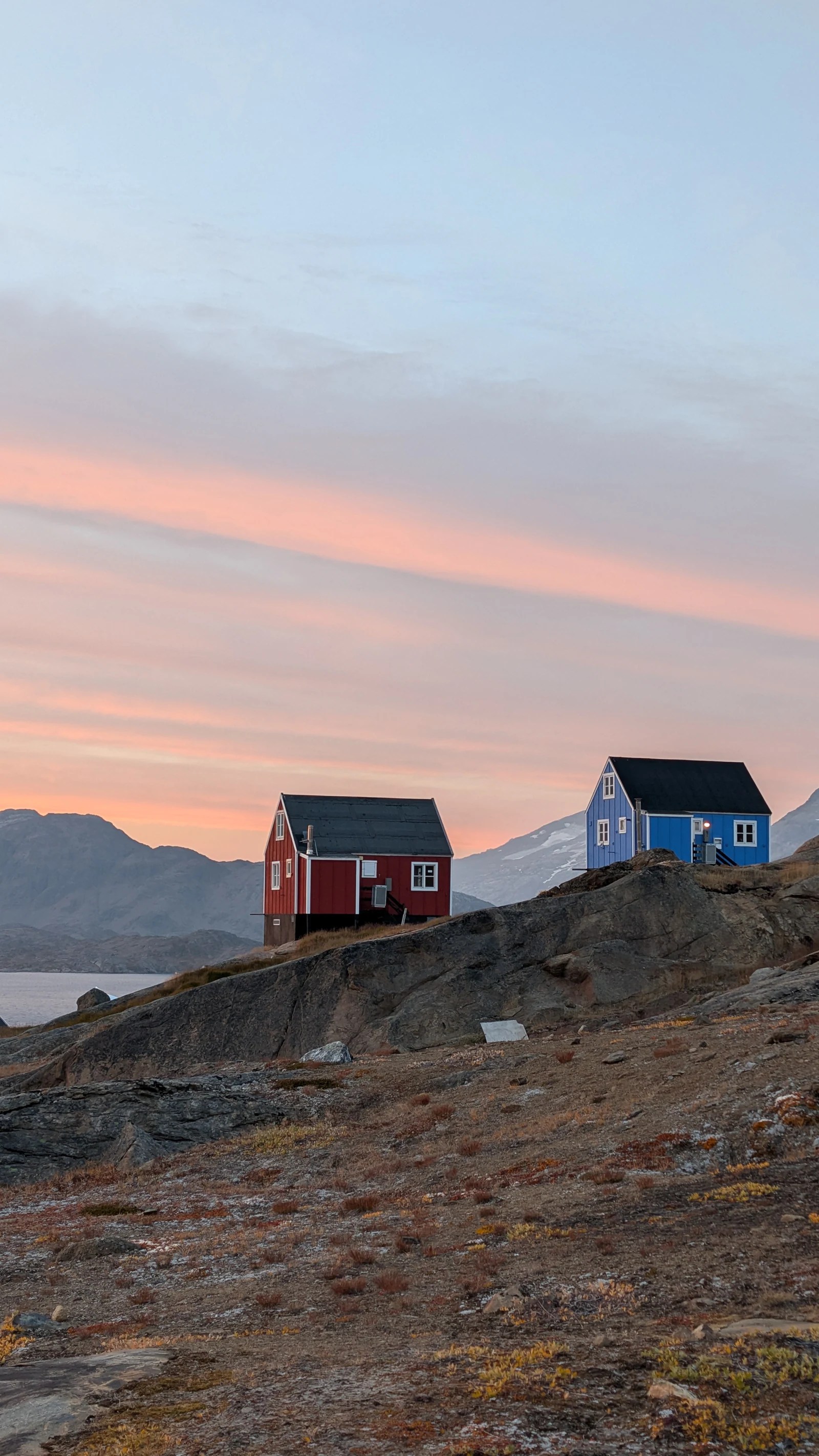 Red and blue houses in Tasiilaq beneath a soft pink evening sky